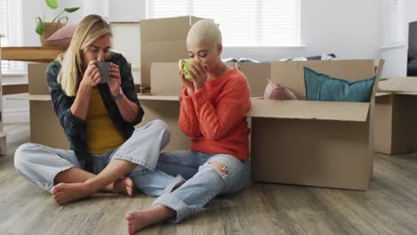 happy diverse female couple with mugs of coffee sitting and moving home