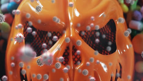 animación de una máscara de halloween naranja con múltiples células de covid 19 flotando y dulces en el fondo