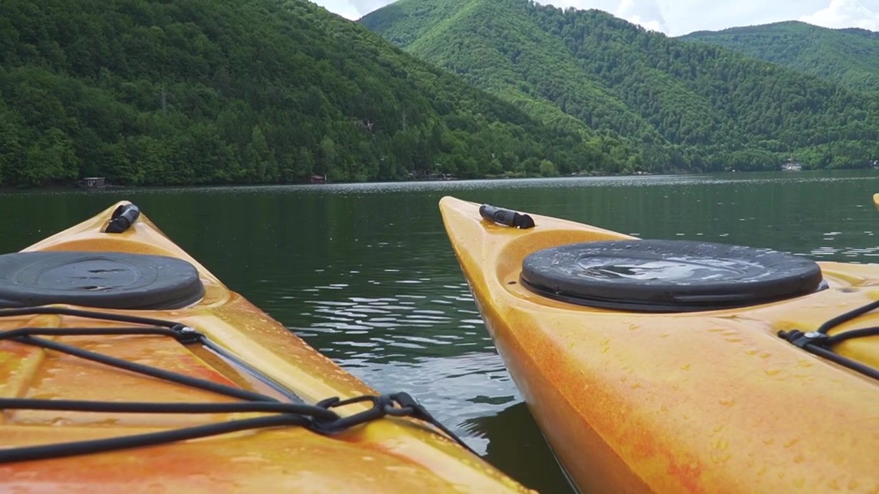 Dos kayaks flotan en un lago tranquilo rodeado de exuberantes montañas verdes. Ideal para temas de aventura al aire libre o videos de viajes