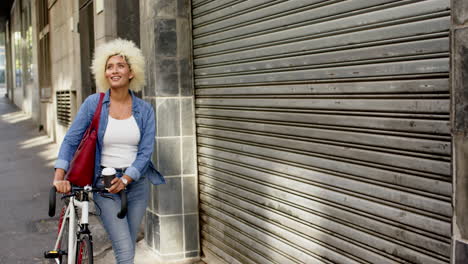 Young-biracial-woman-with-a-bicycle-stands-by-a-metal-shutter-with-copy-space-in-the-city