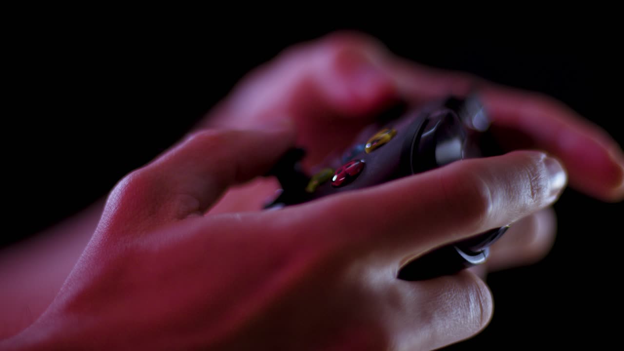 Playing video games in a darkened room with a black background close up on a controller buttons playing quickly soft focus