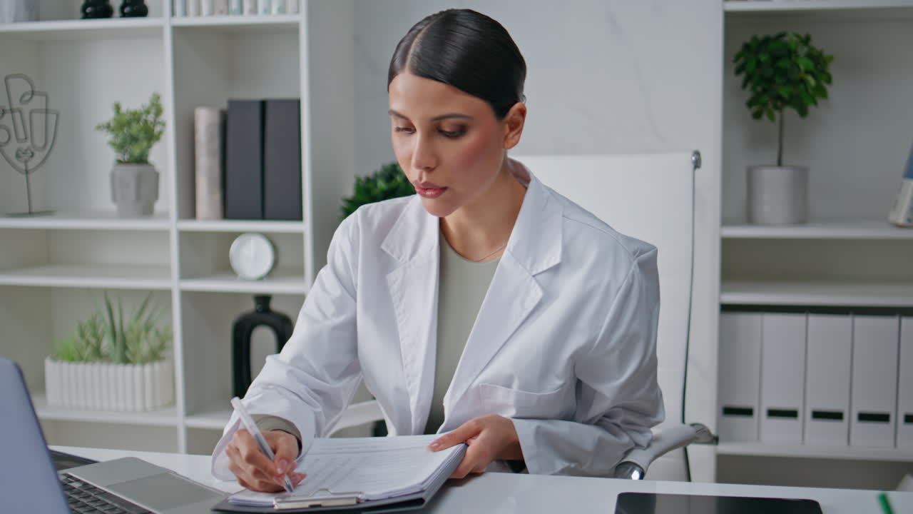 Consultor médico on-line revisando papelada em videoconferência no laptop na clínica