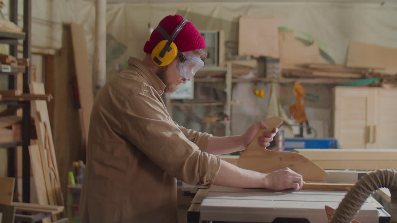 Carpenter in Safety Gear Cutting Plank with Table Saw