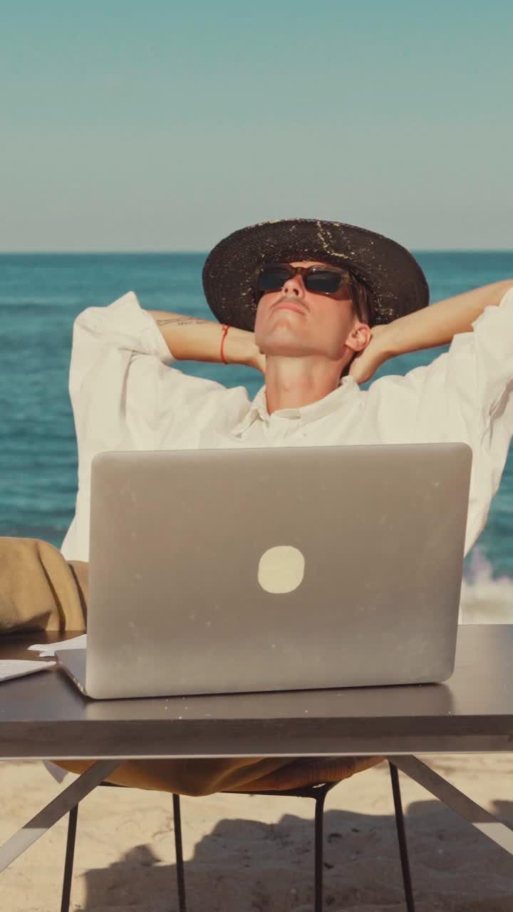 Young caucasian man freelancer resting near table with laptop and sits on beach