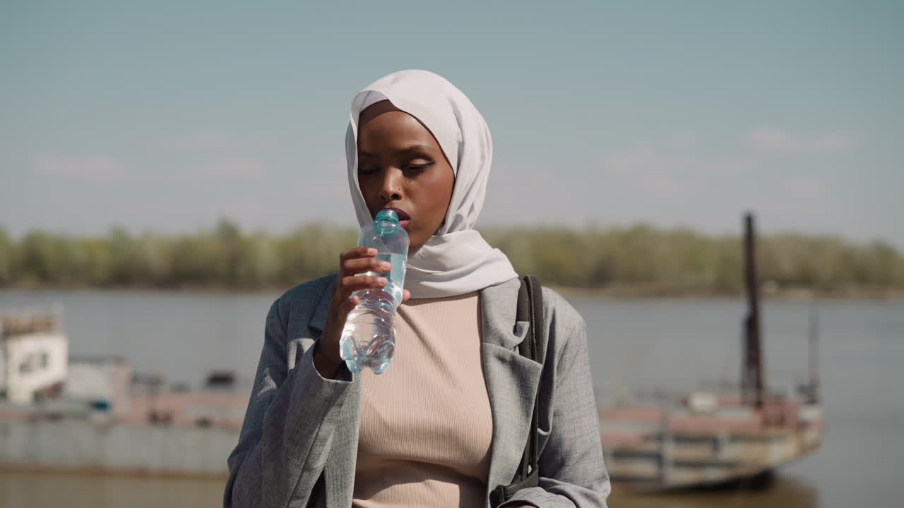 una mujer musulmana cansada abre una botella de agua a la orilla del río