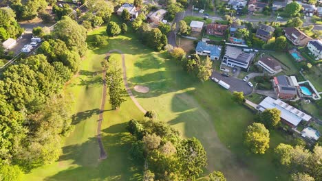 drone footage captures a lush golf course adjacent to a residential neighborhood under bright sunlight