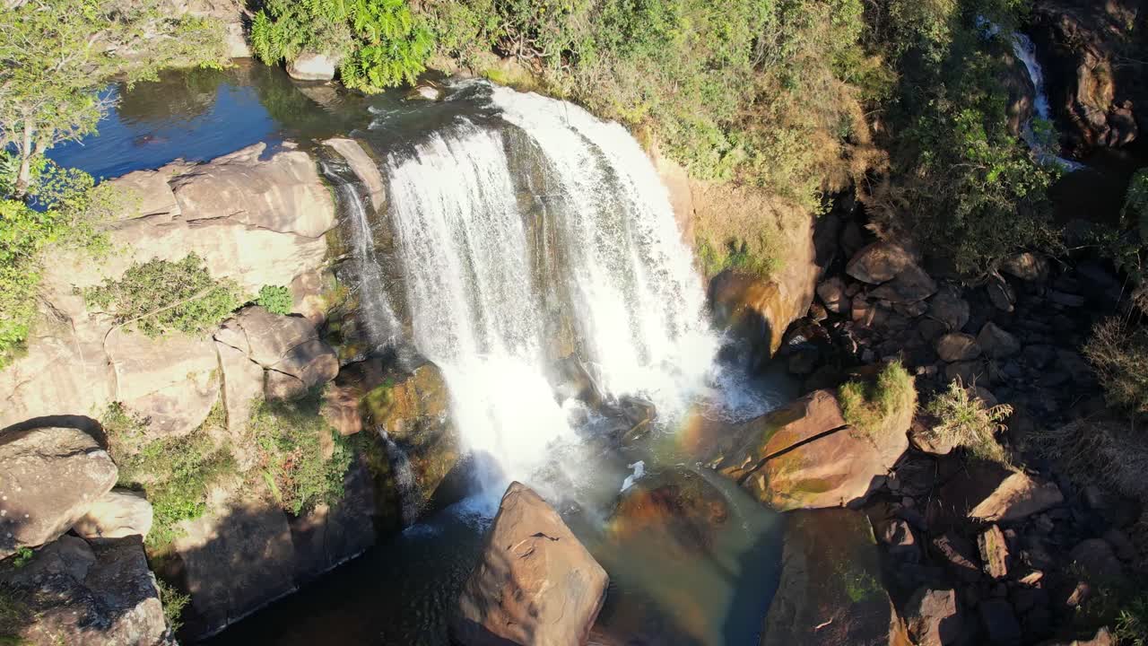 la cámara captura la fuerte caída de la cascada en un día soleado con corrientes de luz que muestran un hermoso y colorido arco iris