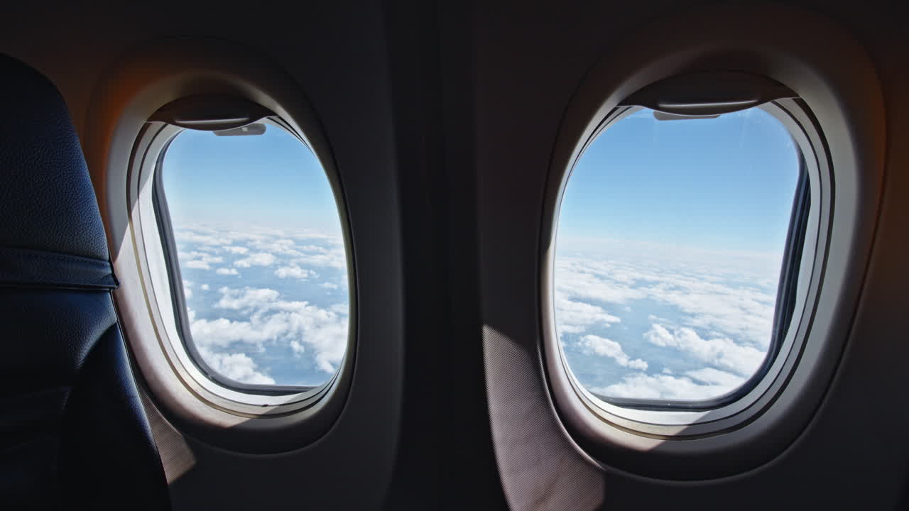 Two airplane windows showing a view of clouds and blue sky from a passenger seat