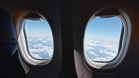 two airplane windows showing a view of clouds and blue sky from a passenger seat