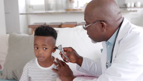 Médico-Afroamericano-Senior-Revisando-El-Oído-De-Un-Paciente-Niño-Con-Otoscopio,-Cámara-Lenta