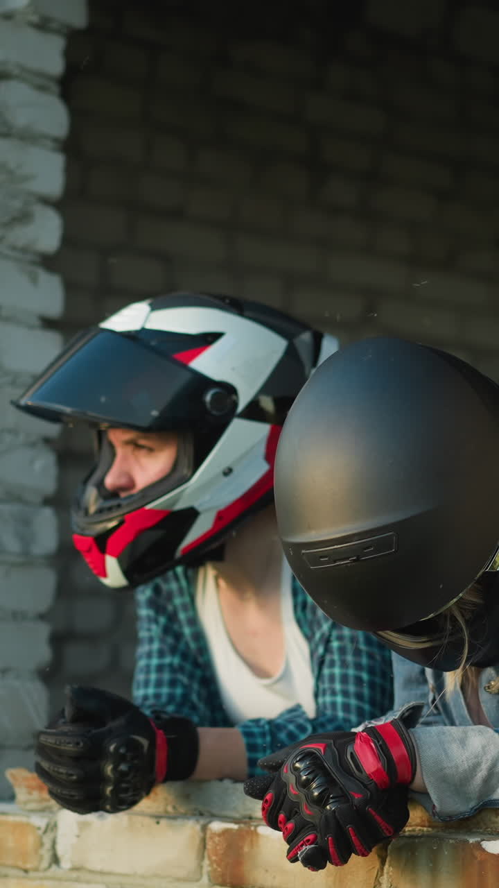 dos mujeres con cascos descansando en la repisa de una ventana de un viejo edificio, una mira pensativa en la distancia mientras la otra mira hacia abajo