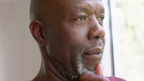 Thoughtful-african-american-senior-man-looking-out-window-at-home,-slow-motion