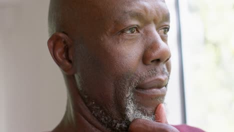 hombre mayor afroamericano pensativo mirando por la ventana en casa, cámara lenta