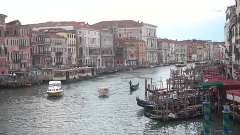 a boat, a vaporetto, and a gondola or canoe sailing through the grand canal of venice, with a promenade on the sides with more gondolas