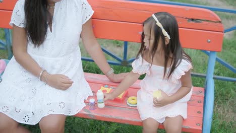 a pregnant mother and her young daughter enjoy playful time together at a playground in the park, surrounded by trees and greenery