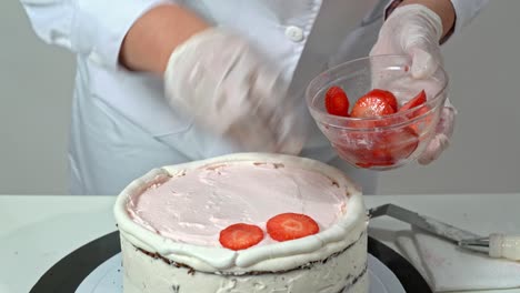 chef placing sliced strawberries on layer of cake that already has some cream on top.