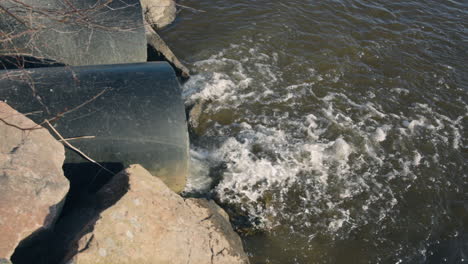 close view of water flowing out of large sewage pipes into lake