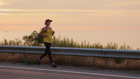 woman makes an evening jog along the road along the lake steadicam follow shot