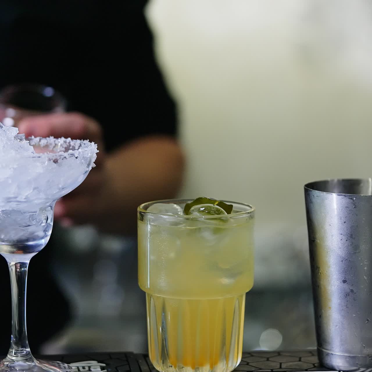 Preparazione di cocktail su un bancone da bar. Un barista mette una foglia verde in un bicchiere pieno di ghiaccio e una bevanda. Primo piano. Sfondo sfocato