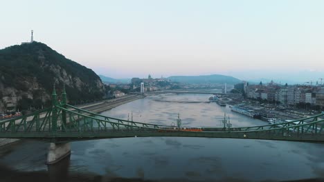 Luftaufnahme-Der-Straßenbahn,-Die-Morgens-Durch-Die-Freiheitsbrücke-über-Die-Donau-In-Budapest-Fährt