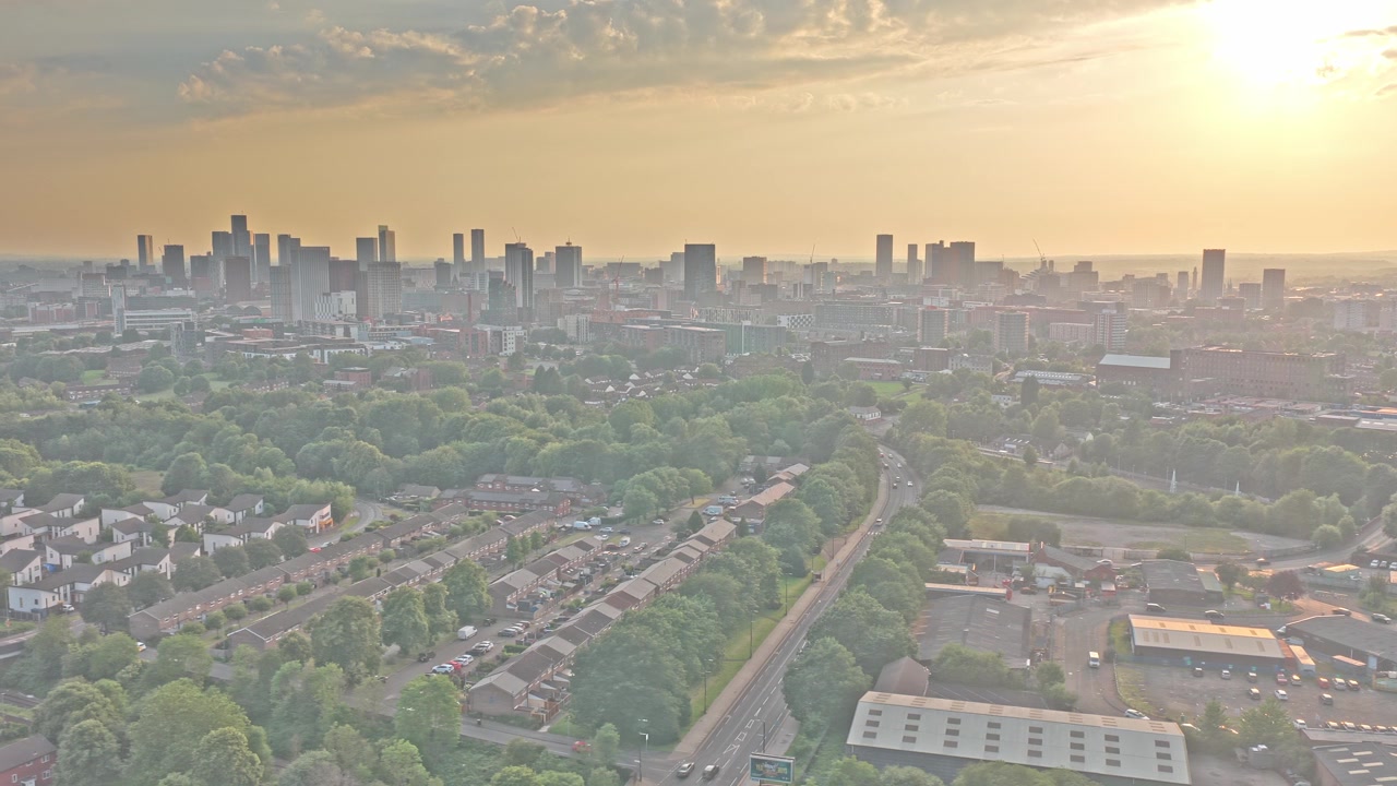 Skyline des Stadtzentrums von Manchester, gesehen von Beswick nahe dem Etihad Campus, Manchester, England, Vereinigtes Königreich, über Wohnvierteln, städtischem Waldgebiet und Verkehrskorridoren, Drohnen-Gleitflug
