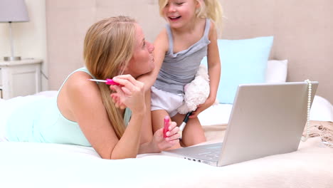 mother and daughter lying on bed using laptop