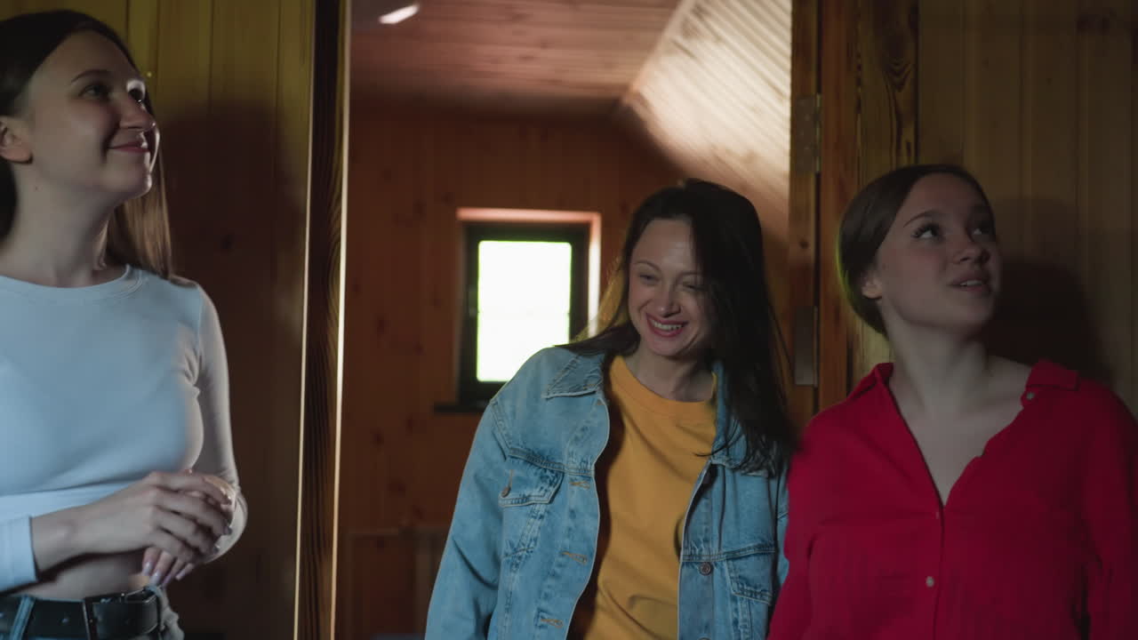 Young woman in red shirt walks into cozy wooden room with soft lighting, pausing to glance around interior with curiosity and mild intrigue, reflecting calm exploration