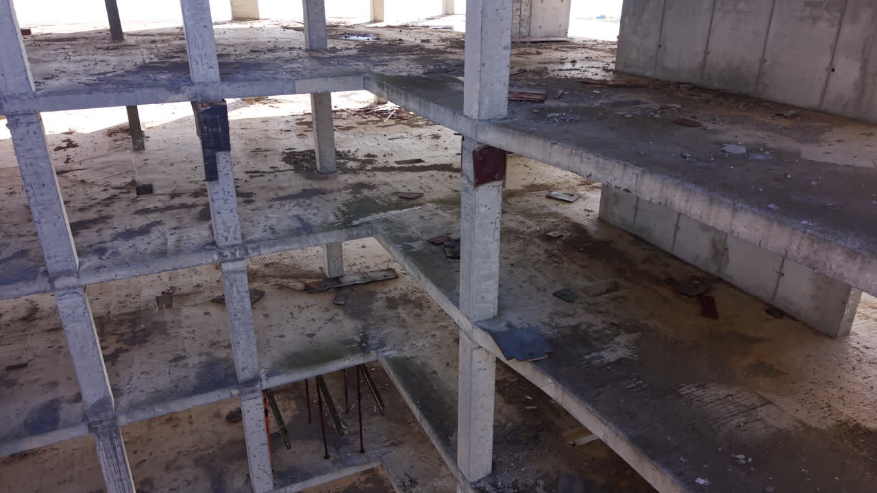 High angle view looking down through a rectangular opening in an unfinished multi-story concrete building. Multiple floors and pillars visible. Aerial