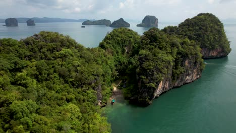 Small-Thailand-tropical-island-with-long-tail-boat-docked,-aerial-pull-back-to-reveal-other-distant-islands--Koh-Lao-Andaman-Sea