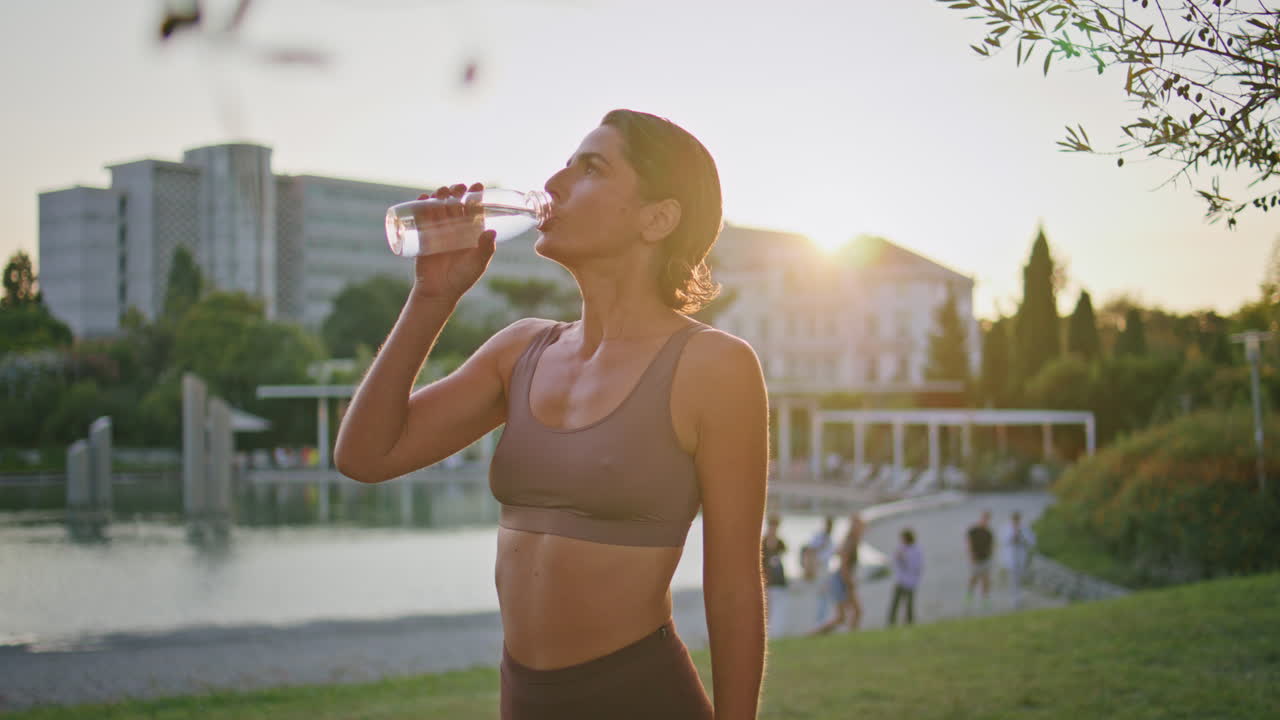 mujer sedienta bebiendo agua parque de fitness entrenamiento de cerca. corredor descanso