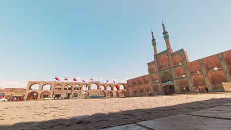 yazd, iran - june 1, 2022: entrance gate and minarets of jameh mosque of yazd, with iranian people and tourists walking