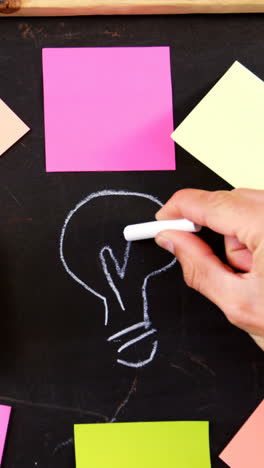 man drawing bulb on chalkboard