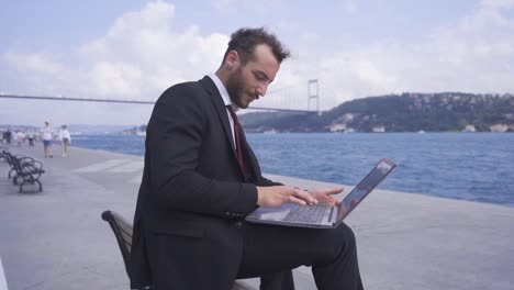 Businessman-sitting-on-the-bench-works-from-his-laptop.-Slow-motion.