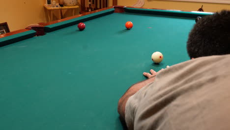 man playing 8 ball pool shoots solid orange 5 ball into corner pocket on a brunswick table with green felt and two balls on the table, open bridge hand and wooden cue stick, no faces perspective angle