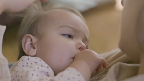 close up shot of an adorable baby girl sucking her thumb and falling asleep while her mother holding her, singing a lullabay and stroking her hair gently 3