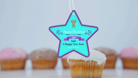 animation of christmas greetings on tag over cupcakes on white background