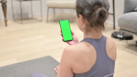 rear view of indian woman using smartphone with chroma screen on yoga mat