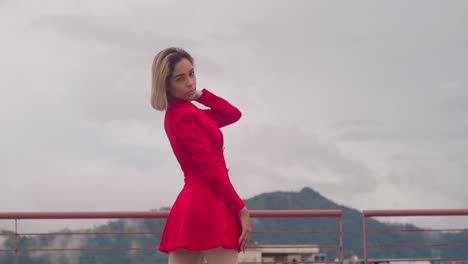 On-a-rooftop-in-Port-of-Spain,-Trinidad,-a-young-Hispanic-girl-wears-a-red-dress,-with-tall-buildings-providing-the-backdrop