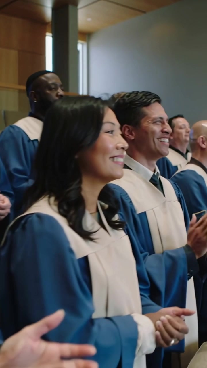 Video verticale: Reagendo a un segnale, coro che applaude e canta in cappella, tuniche blu, stole beige.