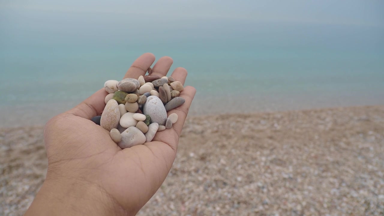 Mano che tiene ciottoli lisci su una spiaggia nebbiosa