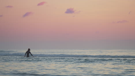 male surfer in silhouette walking in the sea opposite the waves at sunset