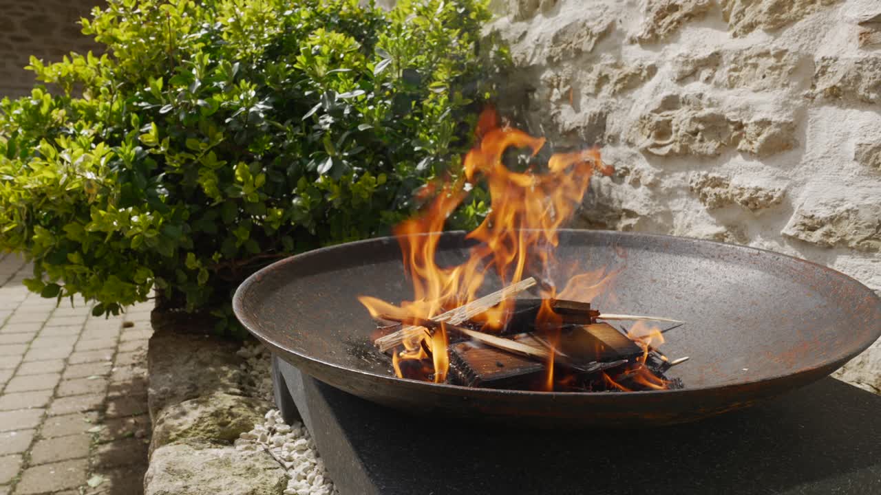 Close up of a hand throwing a stick onto a flame in a cast iron fire pit