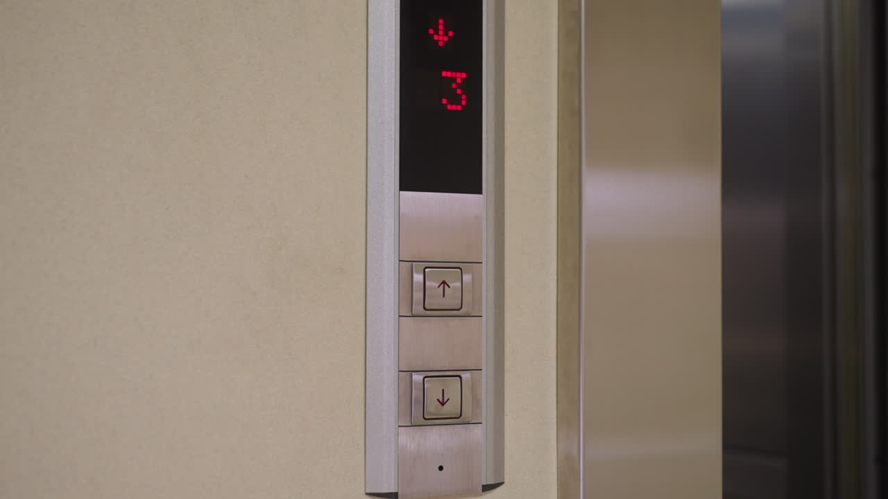 Elevator control panel showing floor number indicator with red digits and up down buttons. Modern metal design with clear display showing floor 3, indicating movement or selection in office building