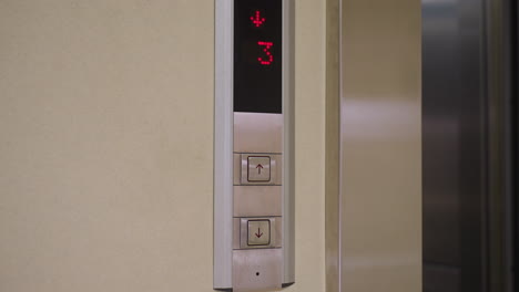 elevator control panel showing floor number indicator with red digits and up down buttons. modern metal design with clear display showing floor 3, indicating movement or selection in office building