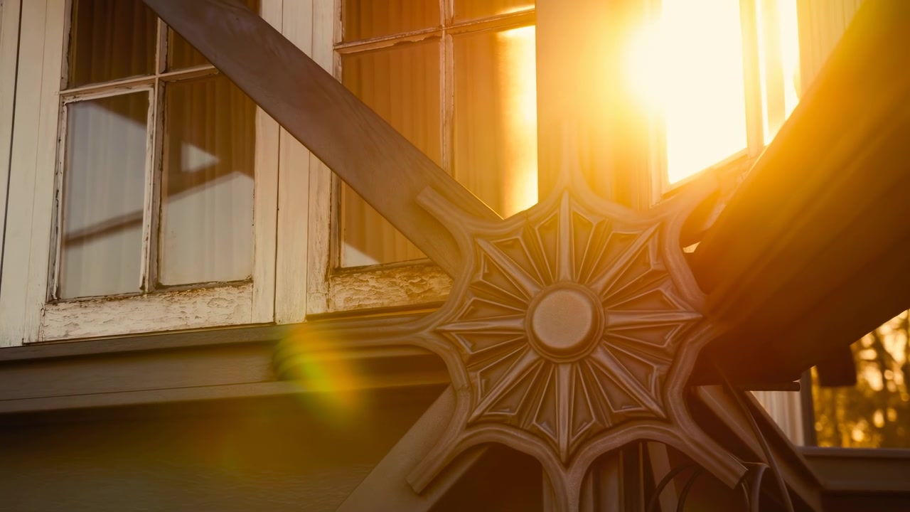 Vista em close-up de um suporte decorativo de metal em forma de estrela montado na parte inferior direita do exterior de um edifício, com caixilhos de janelas de madeira pintados de creme descascando