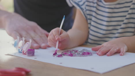 primer plano de padre e hija joven divirtiéndose en casa sentados a la mesa y pintando la decoración juntos - filmado en cámara lenta