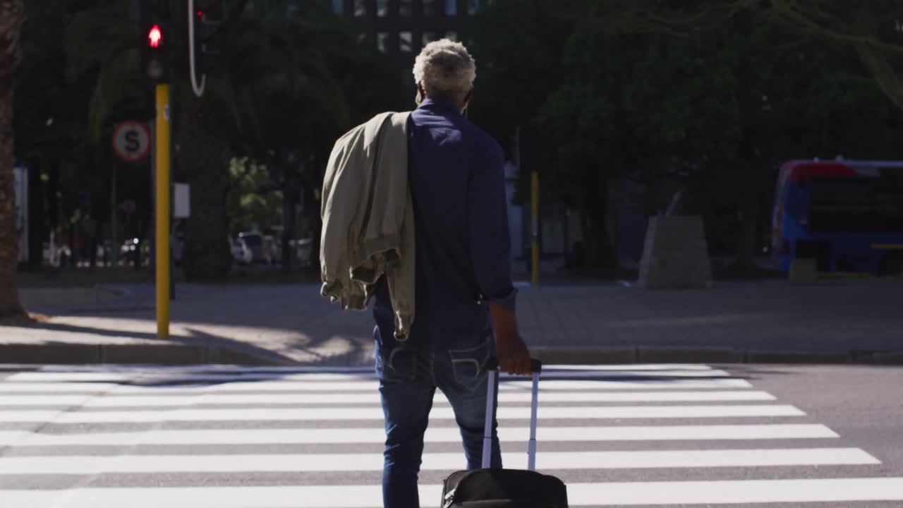 Bagfra set af afroamerikansk ældre mand med trollytaske, der krydser vejen