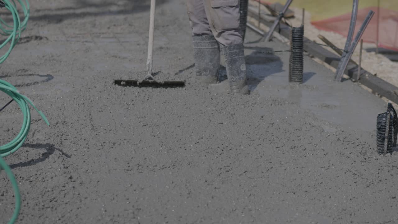 Worker spreading mix of cement and concrete at a construction site, levelling floors