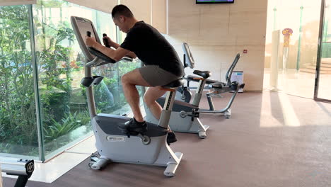 joven masculino asiático pedaleando una bicicleta de ejercicio en un lujoso gimnasio de lujo