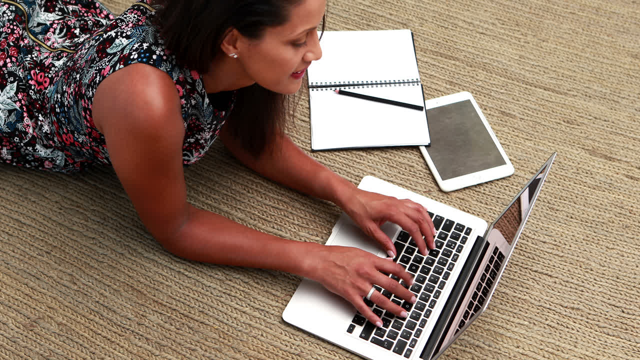 Female executive using laptop while lying on carpet 4k